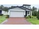 Two-story home with a white two car garage, gray roof, and a brick paver driveway at 877 Rivers Crossings St, Clermont, FL 34714