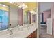 Bright bathroom with double sinks, a large mirror, and a view to an adjacent pink bedroom at 1070 Henley Downs Pl, Lake Mary, FL 32746