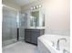 Bright bathroom featuring gray cabinets, dual sinks, soaking tub, and glass-enclosed shower at 16103 Silver Brook Way, Winter Garden, FL 34787