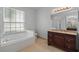Bright bathroom featuring a soaking tub, large window, and a vanity with dark wood cabinets and granite countertop at 548 Casterton Cir, Davenport, FL 33897