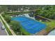 This aerial view showcases a blue tennis court by a pond surrounded by lush landscaping in a well-maintained community at 605 Macglenross Dr, Oviedo, FL 32765