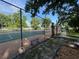 Outdoor tennis court with green and orange surface, surrounded by a chain-link fence and lush trees on a sunny day at 737 Tanglewood Rd, Winter Springs, FL 32708