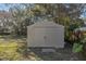 Exterior view of backyard shed with gray metal door and siding, set among shady trees at 11572 Se 60Th Ave, Belleview, FL 34420