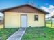 A yellow outbuilding with a white door and window, nestled on a green lawn at 1511 New York Ave, St Cloud, FL 34769