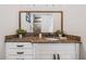Bathroom vanity featuring a granite countertop, decorative mirror, and white cabinets with black hardware at 304 Muirfield Loop, Reunion, FL 34747