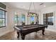 Bright game room with a pool table, pendant lighting, and views of the outdoor balcony through large windows at 304 Muirfield Loop, Reunion, FL 34747
