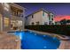 A beautiful backyard pool and spa are illuminated in the evening, with a view of the house and landscaping at 304 Muirfield Loop, Reunion, FL 34747