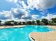 Community pool boasts sparkling water, poolside lounge chairs, and palm trees against a backdrop of blue skies and fluffy clouds at 372 Willet St, Haines City, FL 33844