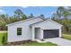 An eye-level shot of a modern home showcases a gray garage door, an entry portal and fresh landscaping at 12197 Sw 76 Ln, Dunnellon, FL 34432