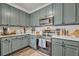 A kitchen features stainless steel appliances and muted green cabinetry with quartz countertops, lovely and bright at 2039 Beachberry Ln, Oviedo, FL 32765