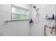 Bright white tiled shower featuring a showerhead, a window, and organized shelving at 1857 E Cooper Dr, Deltona, FL 32725