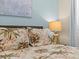 Close up of bedroom features a queen bed with palm tree bedding and gold lamp at 3036 Parrot Head Pl, Kissimmee, FL 34747