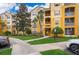 Three-story condo building featuring balconies, vibrant yellow paint, and lush landscaping at 3338 Robert Trent Jones Dr # 203, Orlando, FL 32835