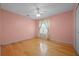 A cozy bedroom with light pink walls, wood flooring, a window with curtains, and a ceiling fan at 4527 Sandhurst Dr, Orlando, FL 32817