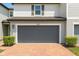 Attached two-car garage with a gray door and a brick driveway with landscape at 1045 Desert Candle Dr, Ocoee, FL 34761