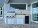 An outdoor kitchen with stainless steel grill, sink, mini-fridge, and white cabinets on a paved patio at 8515 Saint Marino Blvd, Orlando, FL 32836