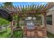 Outdoor kitchen featuring a stone surround, built-in grill, a pergola with climbing vines, and ample counter space at 3188 Verbena Ct, Deltona, FL 32725