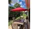 Outdoor patio with a dining table under a red umbrella, surrounded by greenery and landscaping at 1121 Alcove Loop, The Villages, FL 32162
