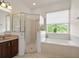 Bathroom featuring a shower with glass doors and a soaking tub near a bright window at 3696 Peacepipe Ct, Clermont, FL 34711