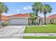 Well-maintained home featuring a red tile roof, a two-car garage, and a lush lawn, enhanced by swaying palm trees at 112 Cordova Ave, Davenport, FL 33897