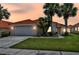 Charming home featuring a red tile roof, palm trees, and a well-manicured lawn against a colorful sunset sky at 112 Cordova Ave, Davenport, FL 33897