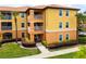 Bright condo building featuring yellow and orange tones, complemented by lush landscaping and palm trees at 5447 Vineland Rd # 1308, Orlando, FL 32811