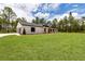 Home exterior featuring attached garage, lush lawn, wooded backdrop, and light-colored modern farmhouse design at 12193 Sw 69 Pl, Ocala, FL 34481