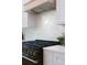 Close-up of a black gas range with gold knobs and white backsplash, complemented by white cabinets and a light wood hood at 13393 Sw 484 Hwy, Ocala, FL 34481