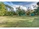 Expansive backyard featuring lush greenery, mature trees, and green outbuildings under a partly cloudy sky at 205 Elaine Pl, Chuluota, FL 32766