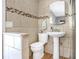 A bathroom featuring tan tiled walls, with a mosaic accent stripe, a pedestal sink and a toilet at 1032 Perkins Rd, Orlando, FL 32809