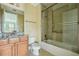 Bright bathroom featuring a shower-tub combo with glass doors, wooden vanity, and neutral tile at 9736 Hatton Cir, Orlando, FL 32832