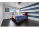 A well-lit bedroom with blue and white striped accent wall, wood floors, and two windows at 10252 Kristen Park Dr, Orlando, FL 32832