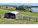 Metal barn structure on a grassy, fenced field near a lake at 16386 Se 156Th Place Rd, Weirsdale, FL 32195