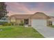Charming single-story home featuring a well-manicured lawn, inviting front entrance, and two car garage at sunset at 10143 Pink Carnation Ct, Orlando, FL 32825