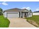 Single-story home featuring a two-car garage, concrete driveway, and a cozy front porch at 123 Zinnia W Ln, Poinciana, FL 34759