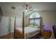 Elegant primary bedroom features a four-poster bed, wood floors and a unique arched window at 8100 Fan Palm Way, Kissimmee, FL 34747