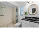 Bright bathroom featuring a standing shower, black marble countertop, and a unique wicker-framed oval mirror at 216 San Fernando Ct, Sanford, FL 32773