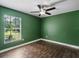 Bedroom with green walls, ceiling fan, wood-style tile floor, and large window for ample natural light at 1391 Terry Ln, Kissimmee, FL 34744