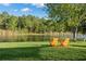 Relaxing waterfront view with two Adirondack chairs on the lush lawn, inviting tranquility and outdoor enjoyment at 14131 Islamorada Dr, Orlando, FL 32837