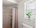 A tiled walk-in shower with neutral tones and a decorative curtain, adjacent to a window with a plant at 315 Pickering Ct, Longwood, FL 32779