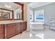 Bright bathroom boasts a soaking tub with lake views, dark wood vanity, and stylish marble flooring at 10845 Bayshore Dr, Windermere, FL 34786