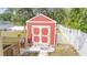 Charming red storage shed with white trim, surrounded by a well-maintained lawn and white fence at 15303 Sw 52Nd Cir, Ocala, FL 34473