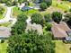 An aerial view of a well-maintained home with a lush green backyard, mature trees, and nearby neighborhood streets at 24720 Calusa Blvd, Eustis, FL 32736