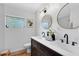 Modern bathroom featuring a dual sink vanity, round mirrors, matte black faucets, and a window for natural light at 5384 Barton Dr, Orlando, FL 32807