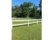 A green pasture enclosed by a bright white fence, surrounded by tall trees and a clear blue sky at 98 Wisteria Dr, Longwood, FL 32779