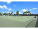 Brightly lit tennis court featuring a net and a fenced perimeter under a sunny sky at 6231 Atkinson Ln, The Villages, FL 32163