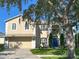 Two-story home with tan stucco, white trim, a blue front door, a large shade tree, and a two-car garage at 1208 Castleport Rd, Winter Garden, FL 34787