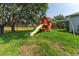 Spacious backyard featuring a large oak tree and a wooden playset with slides and swings at 13108 Lakeshore Grove Dr, Winter Garden, FL 34787