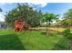 Well-maintained backyard featuring lush grass, a black fence, a papaya tree, and a wooden playset at 13108 Lakeshore Grove Dr, Winter Garden, FL 34787