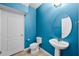 Bright blue half bathroom with a pedestal sink, toilet, and white door at 2193 Betsy Ross Ln, St Cloud, FL 34769